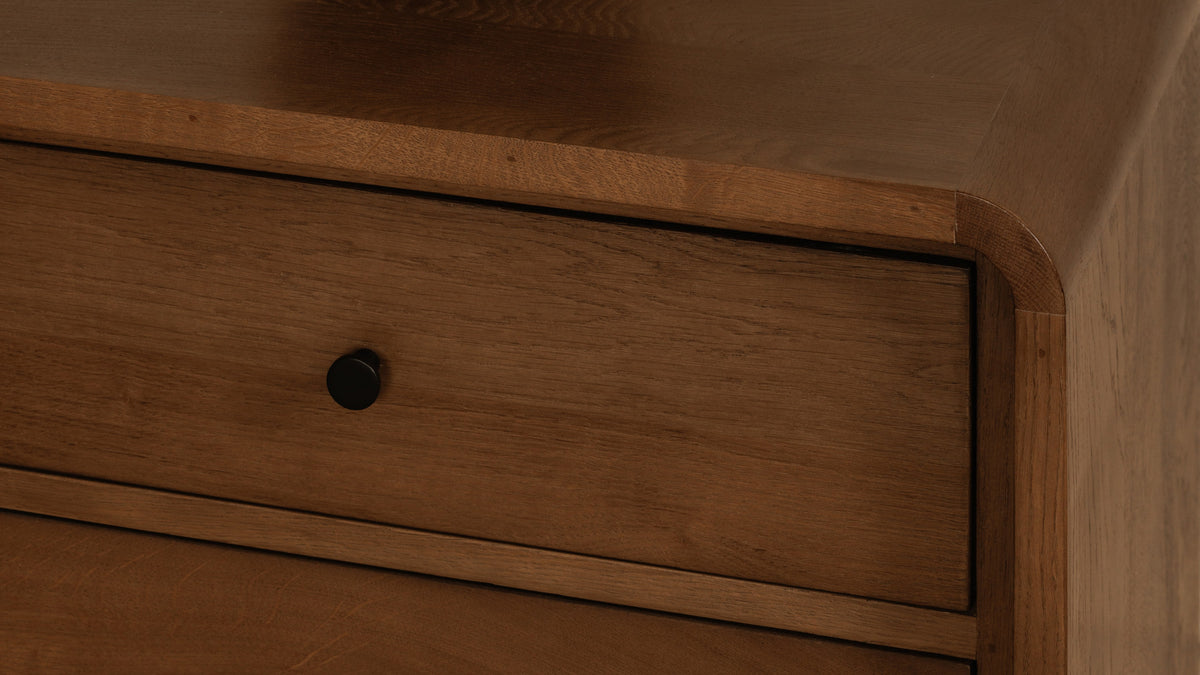Close detail of the Moe's Home Collection Riley nightstand in oak, showing the waterfall edge turning the corner above a drawer front and its small black knob