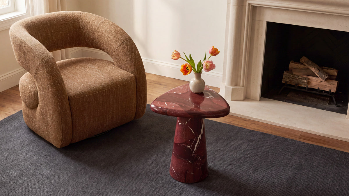 Rodi Side Table in Rosso Levante Marble beside a lounge chair in front of a fireplace