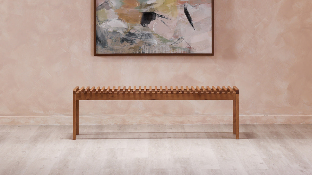 Moe's Home Collection Rohe bench in solid walnut, the full length of its slatted seat seen against a soft pink wall below an abstract painting