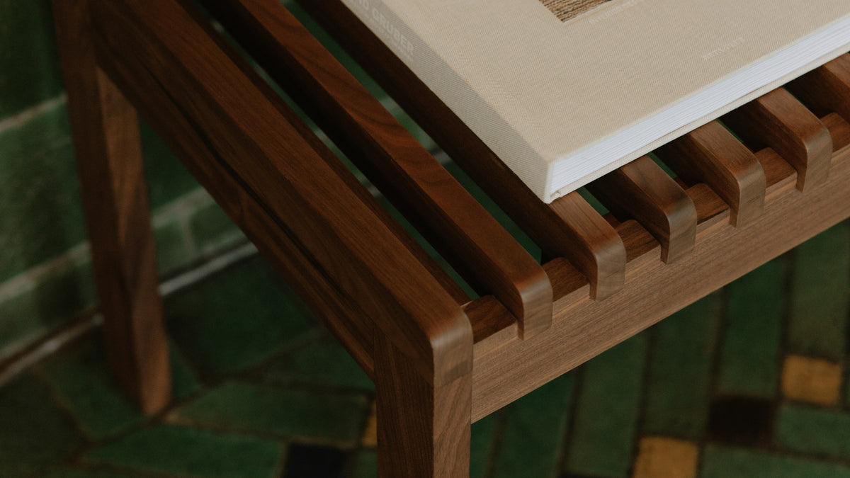 Detail of the Rohe bench's slatted walnut seat with an open book resting across it, green tile behind