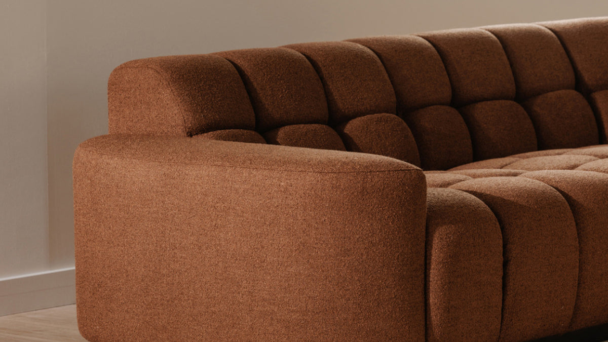 Close view along the Roman L-shaped sectional's wide curved arm in rust upholstery, with the square tufting of the seat and back receding behind it in low daylight