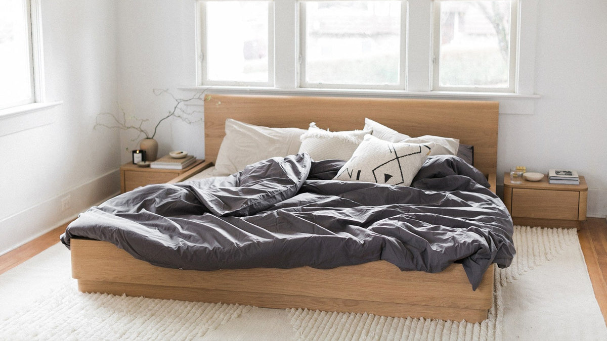 Moe's Home Collection Round Off bed in light oak brown, made up in a bright bedroom with linen shades and a wool rug