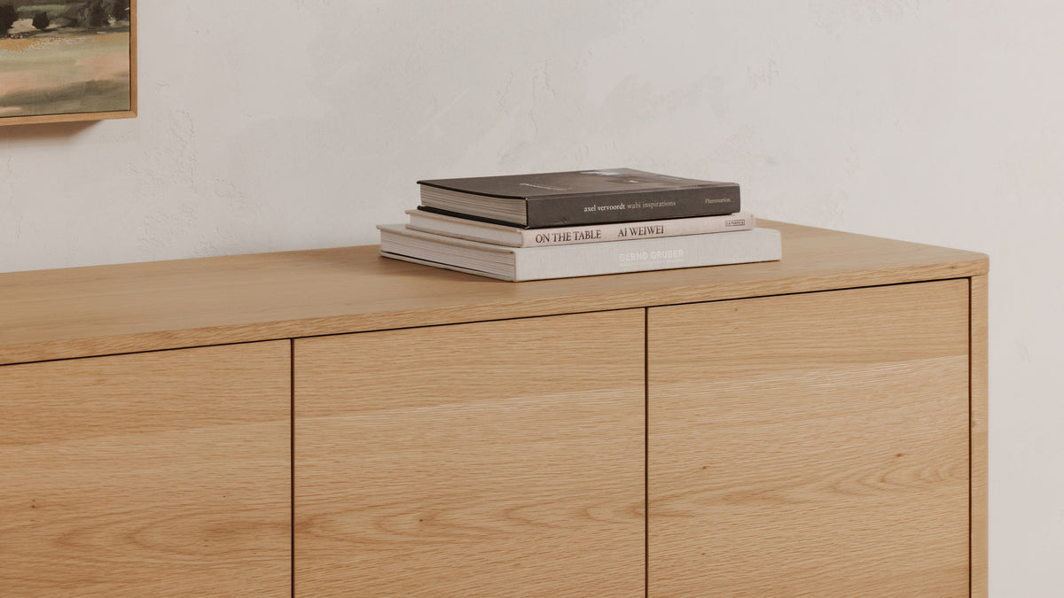 Close view of the Moe's Home Collection Round Off sideboard in natural oak, showing the softened corner and the grain running across the top, with a stack of books resting on it