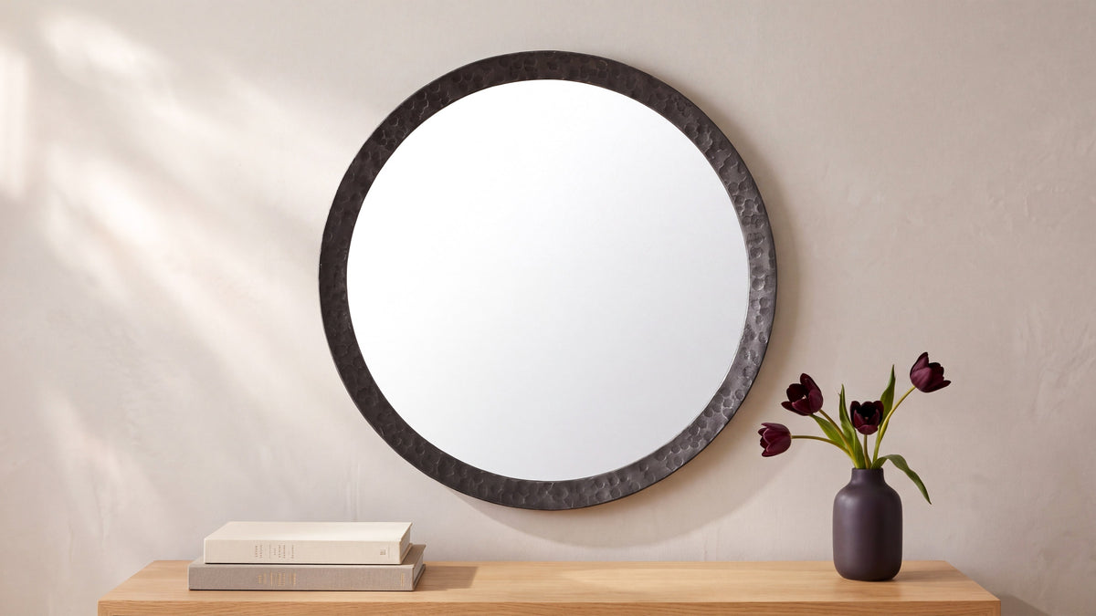 The small Royce mirror in black on a sunlit wall above a light oak console, beside a dark vase holding tulips