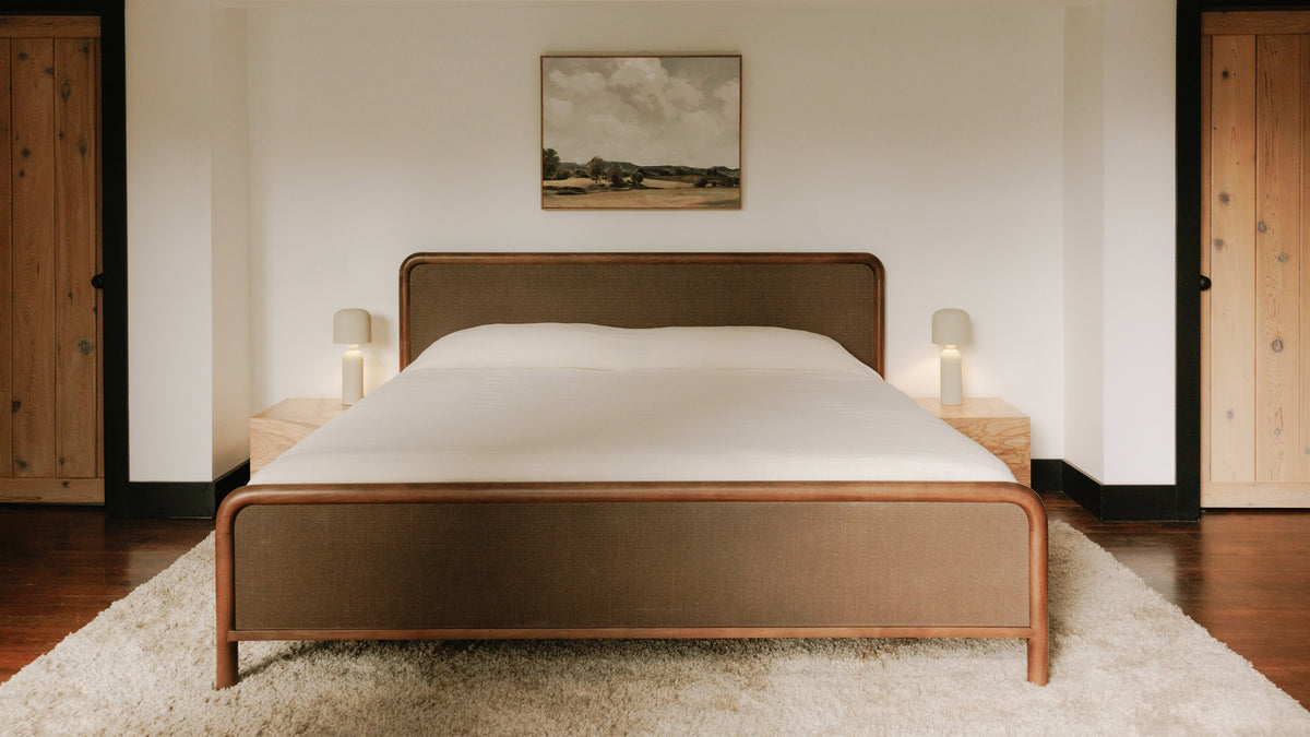 Moe's Home Collection Rye bed in mango wood with woven headboard and footboard panels, made up in white bedding on a cream shag rug, between two small nightstands with cylinder lamps and a framed landscape above