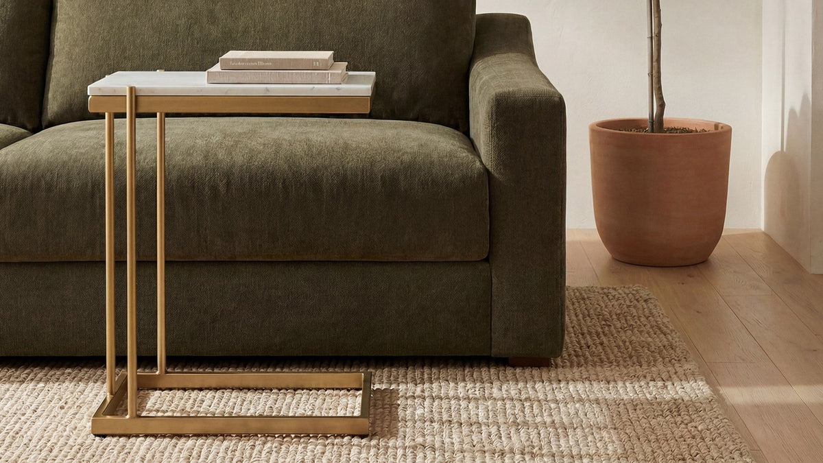 Moe's Home Collection Sulu C table in white marble and gold-finished iron, slid beside a deep green sofa over a jute rug, with books on the marble top