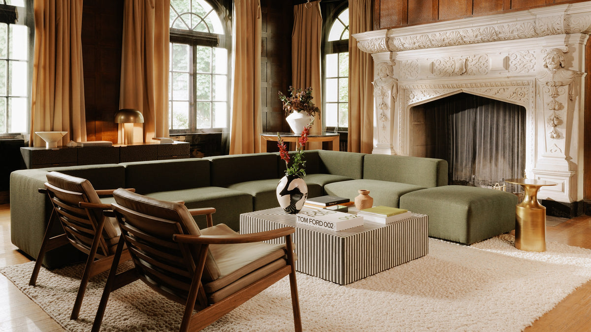 Moe's Home Collection Terning coffee table in black and white bone veneer, styled with art books and a terracotta vase in a panelled living room with a green modular sectional, leather lounge chairs and a carved stone fireplace