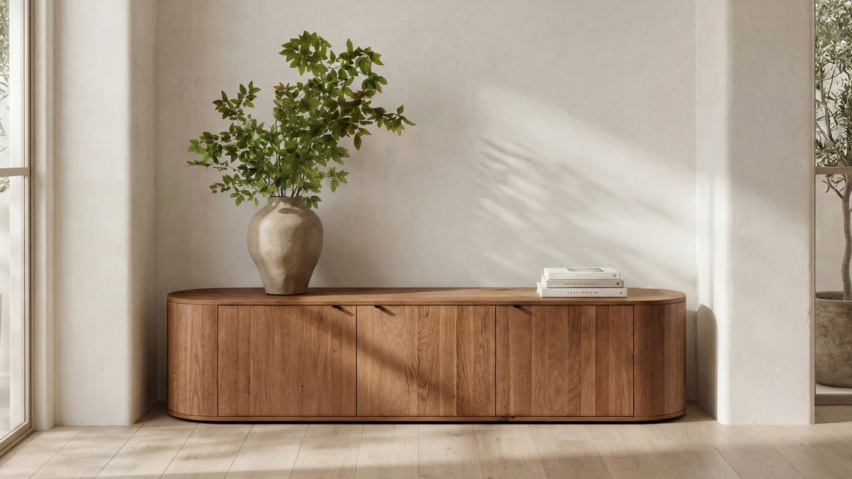 Moe's Home Collection Theo oak media console in a living room, its long rounded case and three doors below a framed abstract painting, two books on its top
