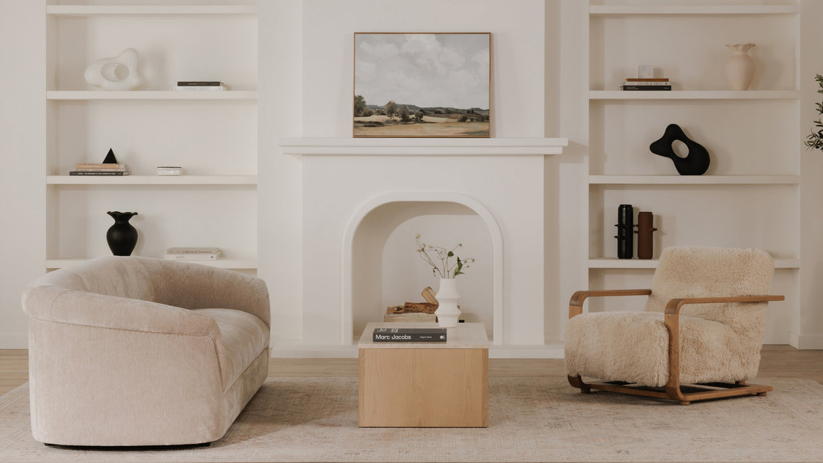 Moe's Home Collection Thora sofa in Beige, seen at an angle in a white room with a plaster fireplace and built-in shelving, across a light-oak block coffee table from a shearling armchair