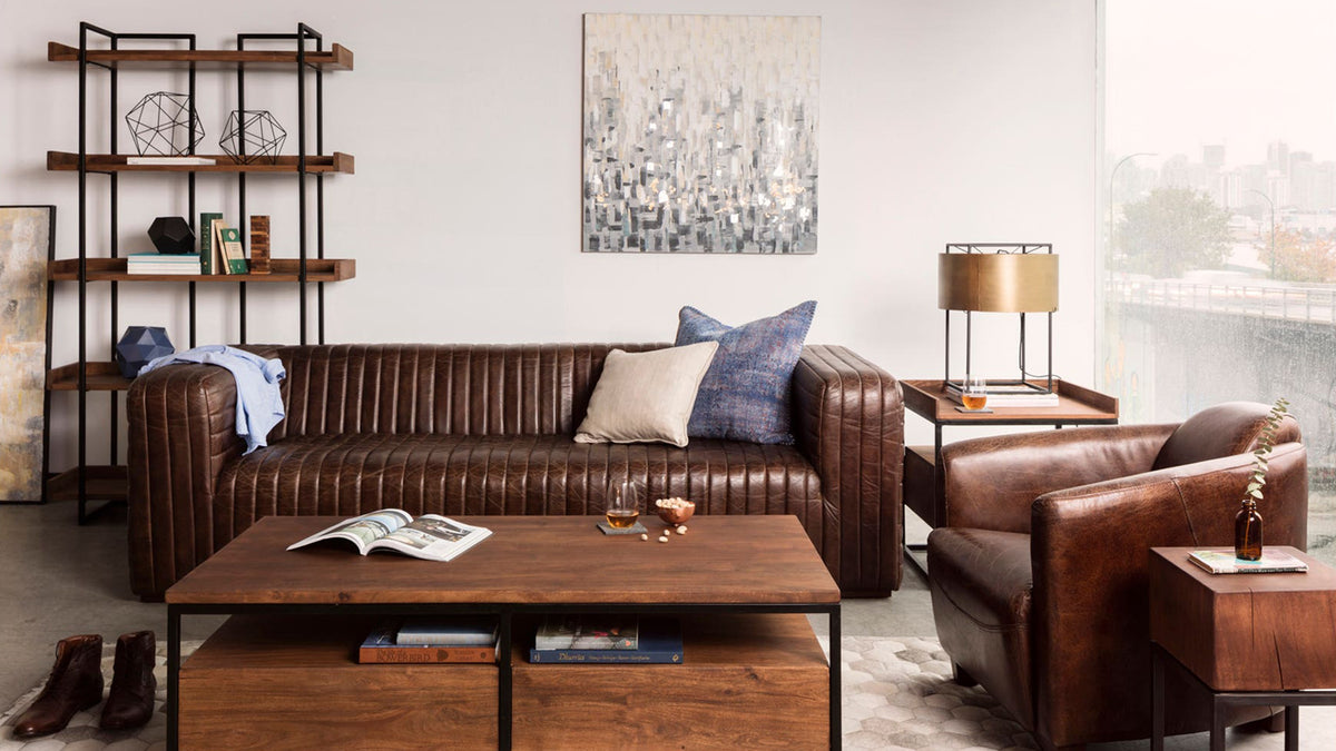 Moe's Home Collection Vancouver Small bookshelf, a black iron frame carrying solid acacia shelves of books and objects, beside a brown leather sofa and a wood coffee table