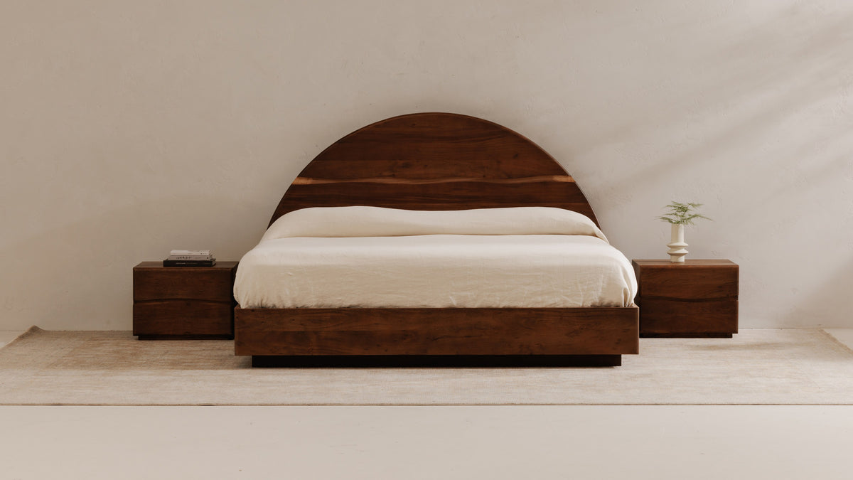 Moe's Home Collection Watson bed in walnut-finished acacia with an arched headboard, made up in cream bedding on a pale rug between two walnut nightstands against a plaster wall