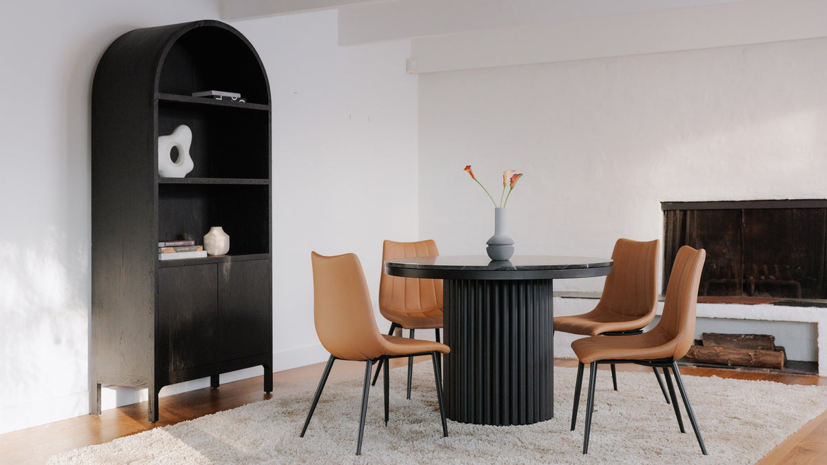 Moe's Home Collection Wilde display cabinet in black oak, arched, with an open upper shelf, in a dining room with tan leather chairs and a black pedestal table