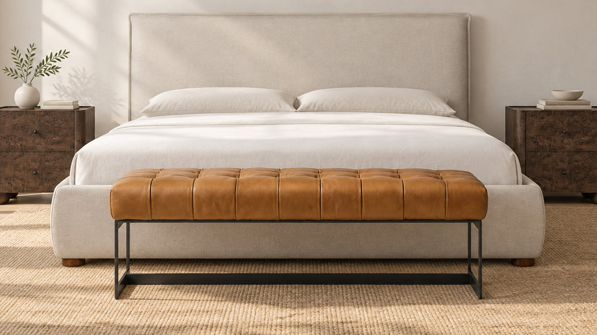 Moe's Home Collection Wyatt bench in tan top-grain leather on a black iron base, at the foot of a cream upholstered bed on a natural-fibre rug
