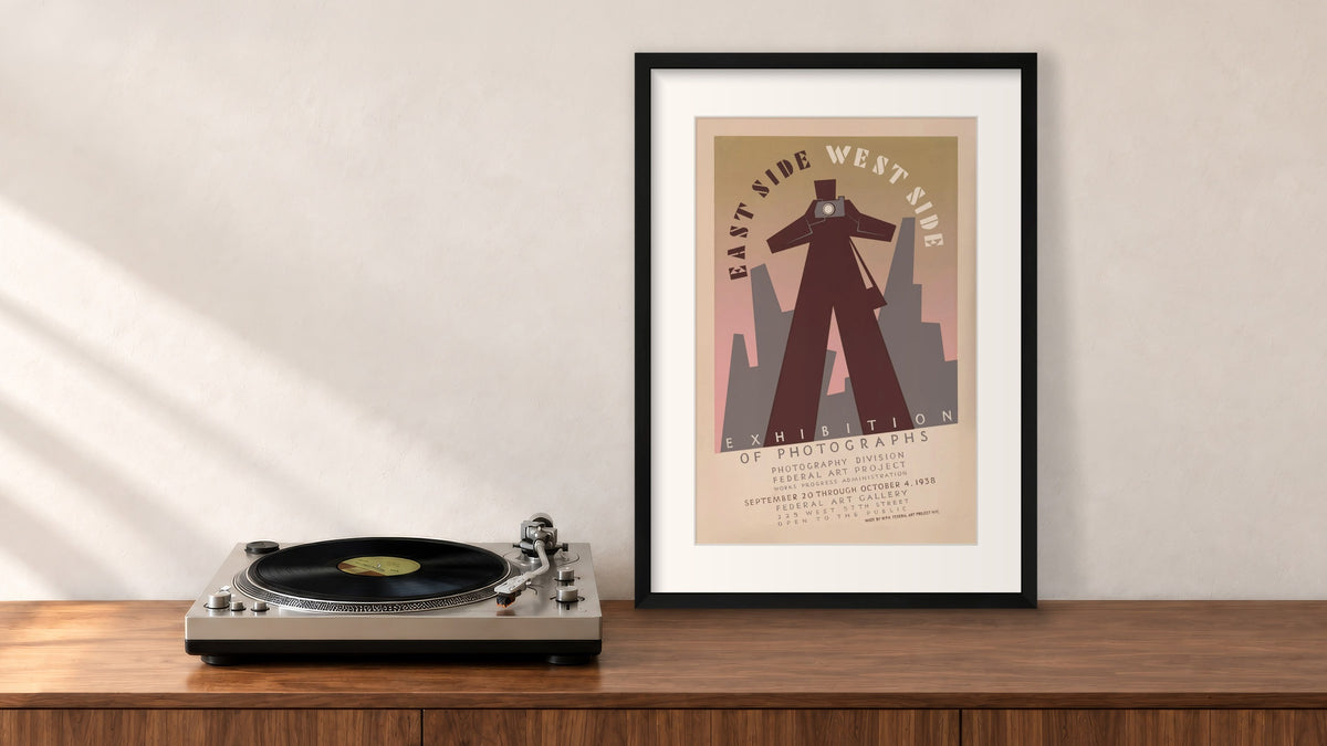 East Side West Side Framed Print in a black frame, leaning on a walnut console beside a turntable